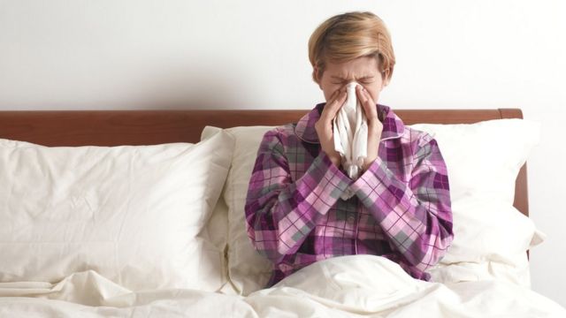 Woman lying on bed in pajamas blowing her nose into a handkerchief.