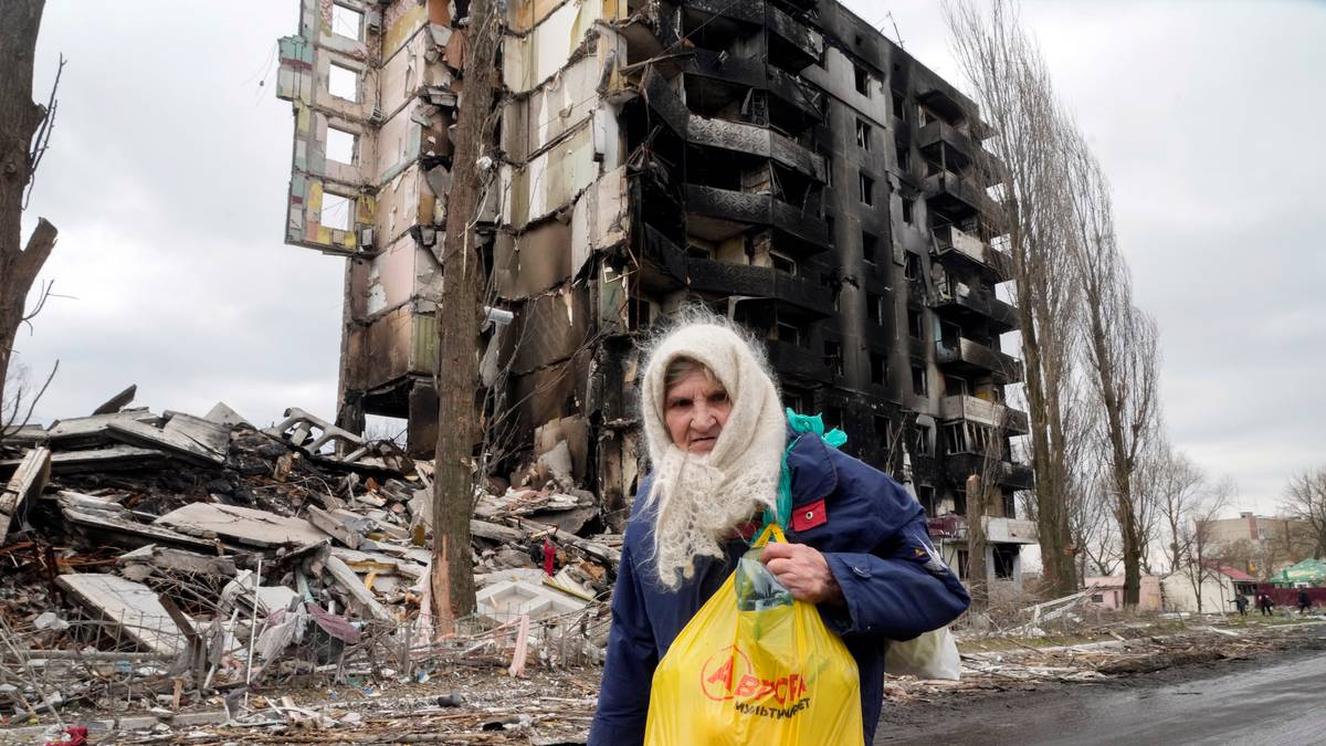 En kvinne går foran to utbrente boligblokker i Borodjanka i Ukraina 6. april